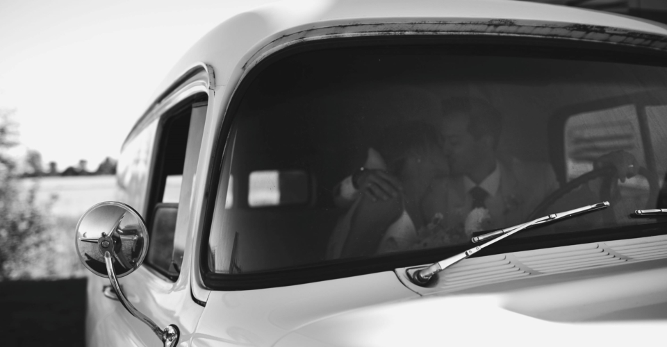Black and white photo of bride and groom kissing in old car at Mackinnon Brewery